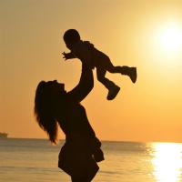 Frau, Die Baby Am Strand Während Des Sonnenuntergangs Trägt